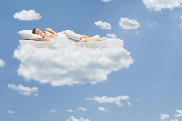 Young woman sleeping on a floating mattress up in the clouds and a blue sky