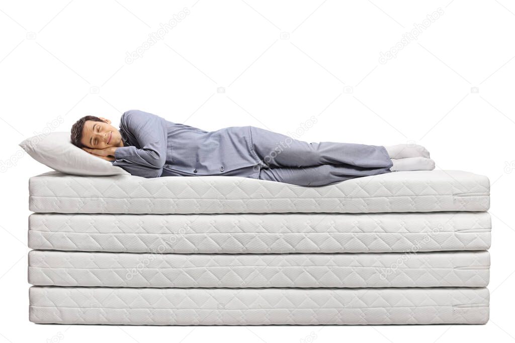Full length shot of a young man sleeping peacefully on  a pile of soft mattresses isolated on white background