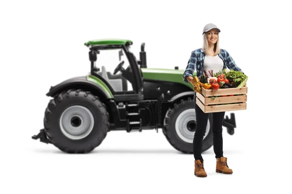 白を基調としたトラクターの前に野菜を乗せた箱を持った若い女性農家の全長の肖像画 — ストック写真