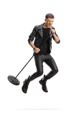 Beyaz arka planda izole edilmiş bir mikrofonla atlayan genç erkek rock şarkıcısı.