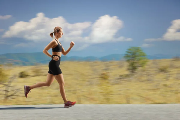 一名健康的年轻女子在一条大路上慢跑时的全长侧面照 — 图库照片