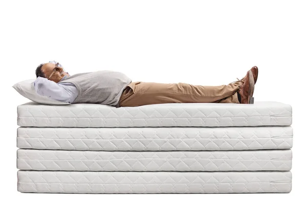 一个成熟的男人躺在一堆被白色背景隔开的床垫上 — 图库照片