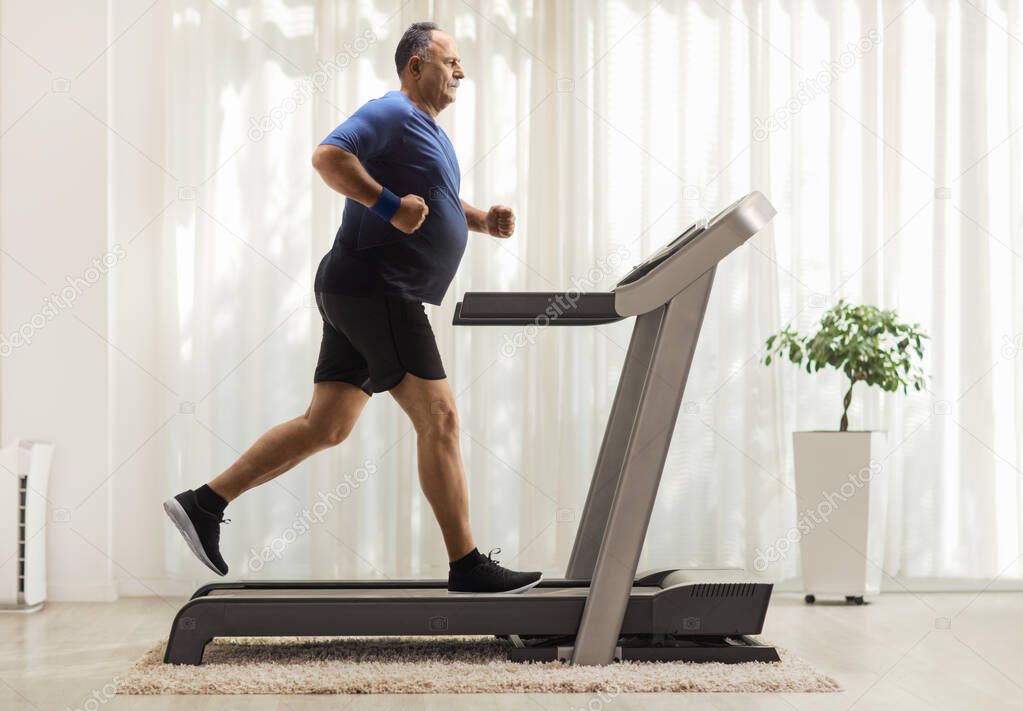 Full length profile shot of a mature man running on a treadmill in a room 