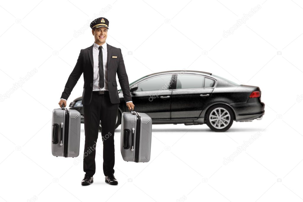 Full length portrait of a chauffeur in a uniform carrying suitcases in front of a black car isolated on white background