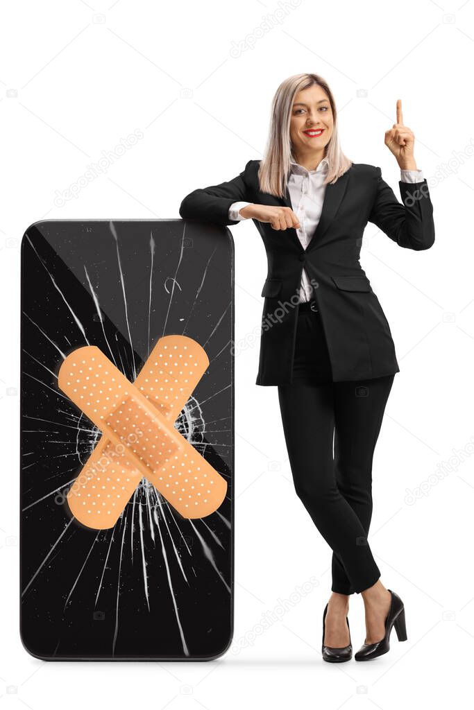 Full length portrait of a young businesswoman leaning on a cracked smartphone with bandage and pointing up isolated on white background