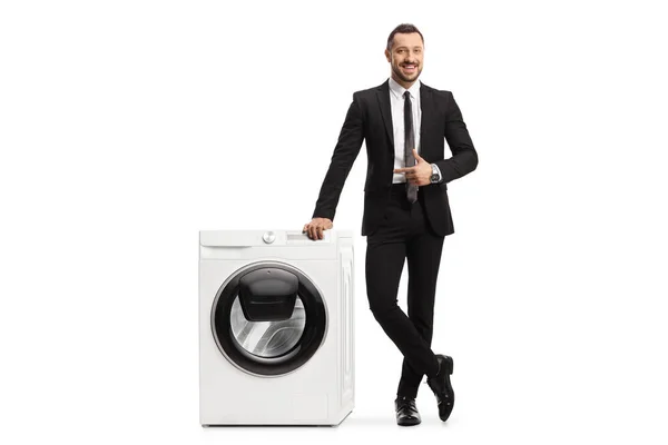 洗濯機にもたれて白い背景に隔離されたスーツの若いプロの男の完全な長さの肖像画 — ストック写真