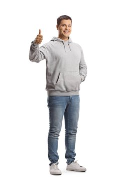 Gri kapüşonlu ve kot pantolonlu genç bir adamın beyaz arka planda parmaklarını gösteren uzun bir portresi.