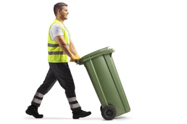 Beyaz arkaplanda izole edilmiş plastik bir çöp kutusunu iten bir çöp toplayıcısının tam uzunluktaki profil görüntüsü