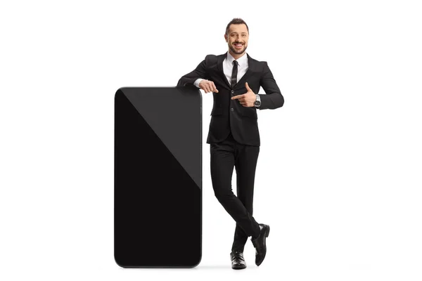 大きなスマートフォンの横に立って白い背景に隔離された若いプロの男の完全な長さの肖像画 — ストック写真