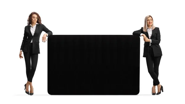 Due Giovani Imprenditrici Appoggiate Grande Pannello Nero Isolato Sfondo Bianco — Foto Stock