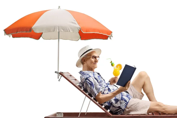 上了年纪的男人躺在日光浴床上 拿着一本书和一杯酒 背景是白色的 — 图库照片