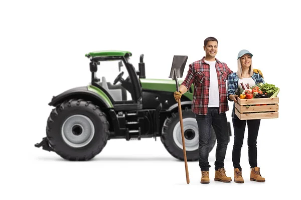 ショベルを持つトラクターと白を背景に隔離された野菜とクレートを持つ男性と女性の農家の完全な長さの肖像画 — ストック写真