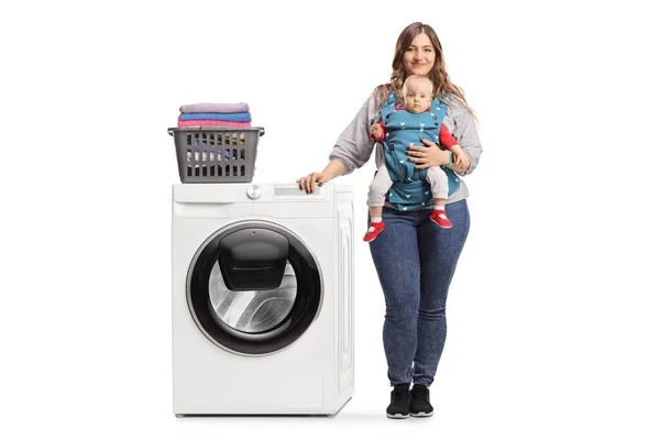 白い背景に隔離された洗濯機にもたれている赤ん坊を持つ母親の完全な長さの肖像画 — ストック写真