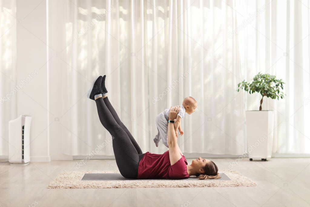 Young mother exercising abs and holding a baby on the floor at home