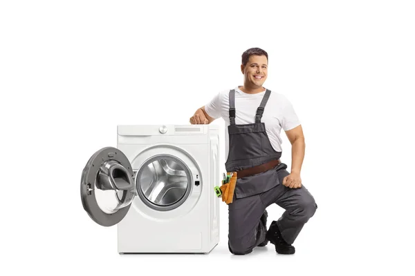 修理工跪在洗衣机旁边 看着被白色背景隔离的相机 — 图库照片