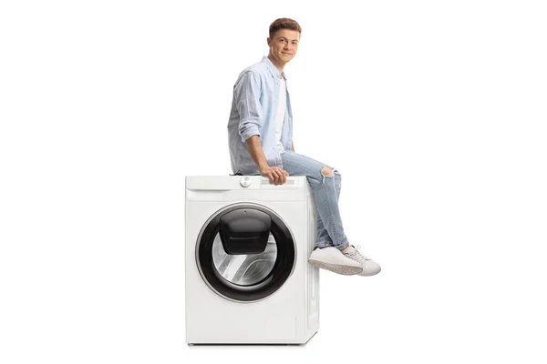小伙子坐在洗衣机上 看着被白色背景隔离的相机 — 图库照片