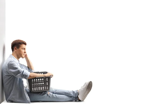 一个人坐在墙上 靠着一个被白色背景隔开的洗衣篮 — 图库照片