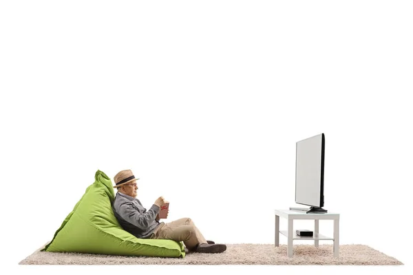 老人坐在豆袋椅子上 看电视 吃着被白色背景隔开的爆米花 — 图库照片