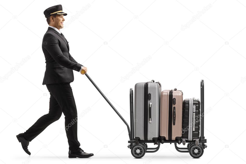 Full length profile shot of a bellboy walking and pushing a trolley cart with suitcases isolated on white background