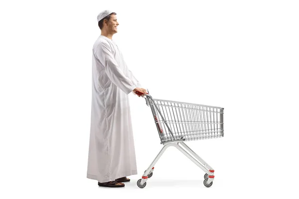 白い背景に隔離された空のショッピングトロリーを持つ民族服の男の完全な長さのプロフィールショット — ストック写真