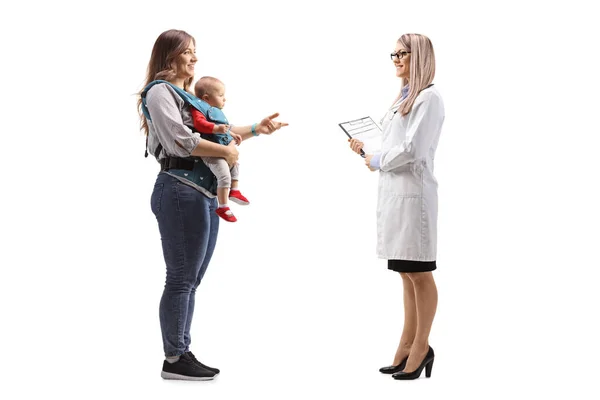 キャリアの赤ん坊を持つ母親と白い背景に隔離された会話を持つ女性医師の完全な長さのプロフィール写真 — ストック写真