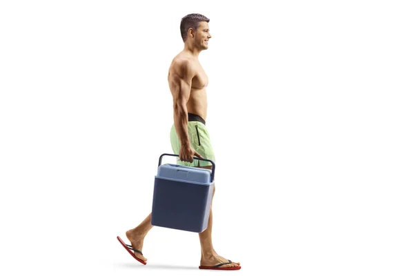 フル長さプロフィールショットの若いです男で水泳パンツ保持ポータブル冷蔵庫と歩行孤立した上の白い背景 — ストック写真