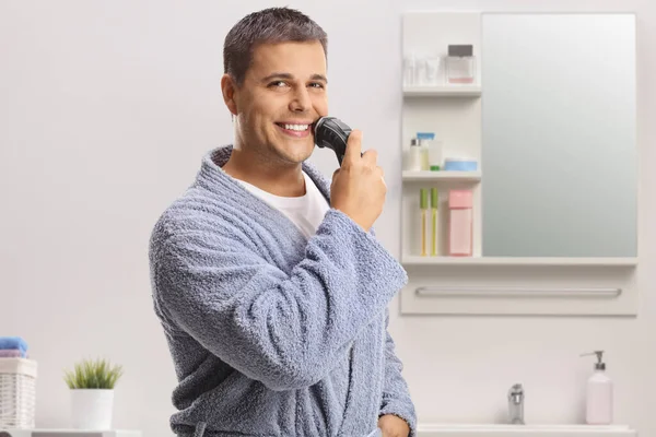 Genç Adam Banyoda Tıraş Makinesi Kullanıyor Kameraya Gülümsüyor — Stok fotoğraf