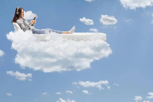 ベッドに寝そべって空に浮かぶヘッドフォンを持つ女性 — ストック写真