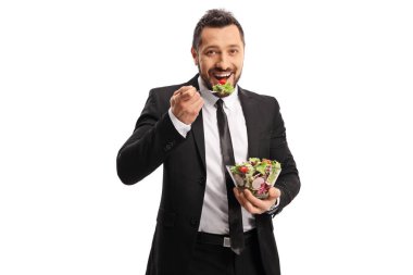 Takım elbiseli ve kravatlı bir iş adamı beyaz arka planda izole edilmiş taze bir salata yiyor.