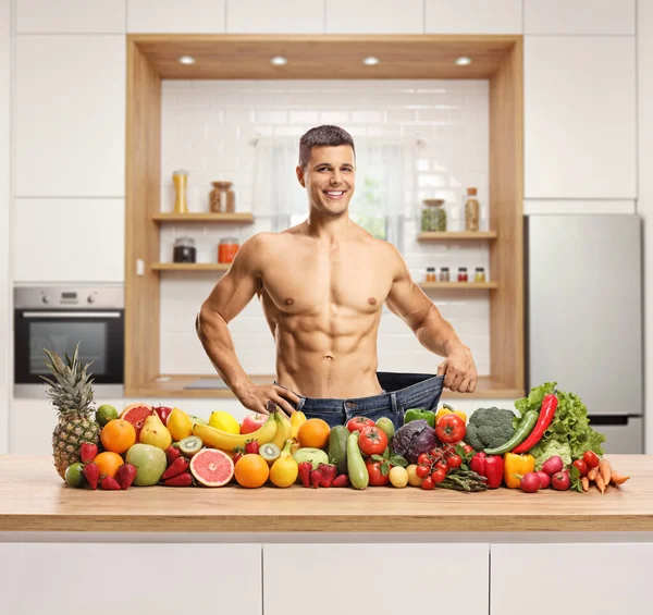 在厨房柜台后面摆弄着一堆水果和蔬菜 穿着大号牛仔裤的男人 — 图库照片