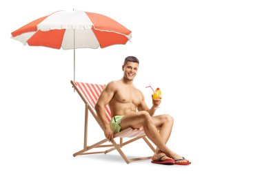 Yüzme şortlu bir adam şemsiyenin altında bir plaj sandalyesinde oturuyor ve elinde beyaz arka planda izole edilmiş bir kokteyl tutuyor.