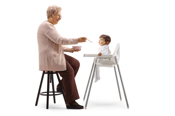 Avó Alimentando Bebê Uma Cadeira Isolada Fundo Branco — Fotografia de Stock