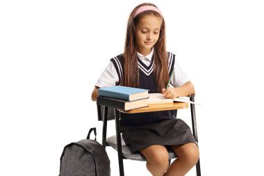 Female pupil in a school uniform sitting and writing school work isolated on white background clipart