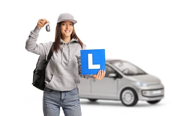 在白色背景下隔离的银色汽车上拿着学习车牌和汽车钥匙的女青少年 — 图库照片