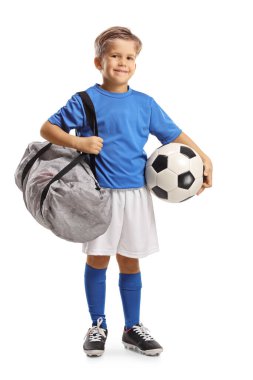 Spor formalı, elinde bir futbol topu ve beyaz arka planda izole edilmiş bir spor çantası olan küçük bir çocuğun tam boy portresi.
