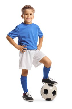 Beyaz arka planda izole edilmiş bir futbol topuna basan spor formalı mutlu küçük çocuk.