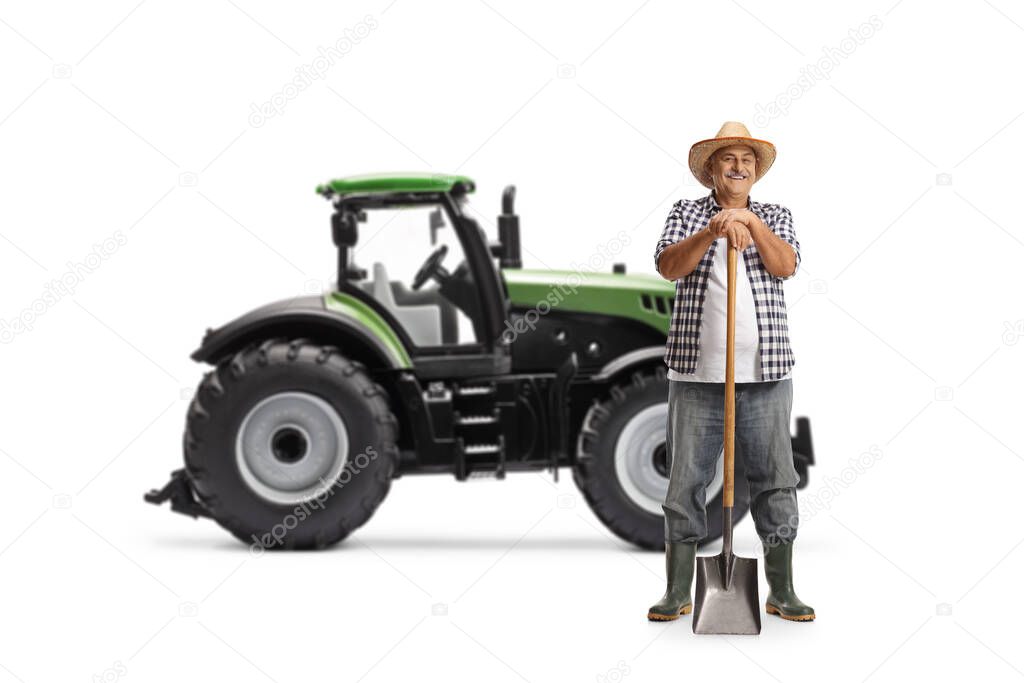 Full length portrait of a mature farmer posing with a shovel in front of a tractor isolated on white background