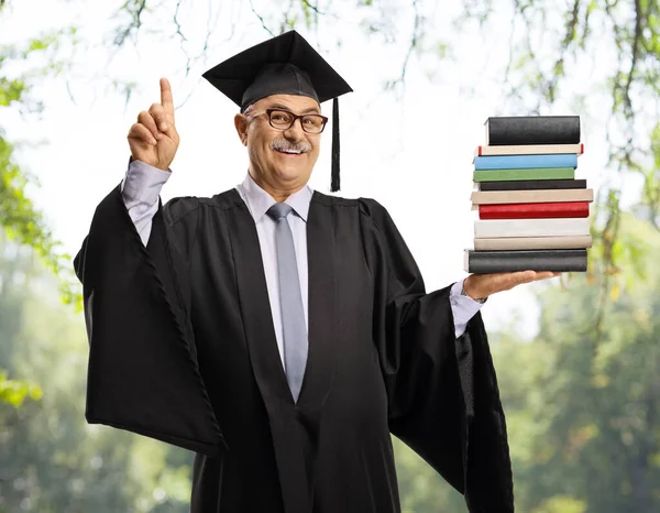 Hombre Maduro Feliz Vestido Graduación Sosteniendo Una Pila Libros Apuntando — Foto de Stock