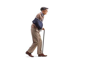 Beyaz arka planda sopayla yürüyen yaşlı bir adamın tam boy profil fotoğrafı.
