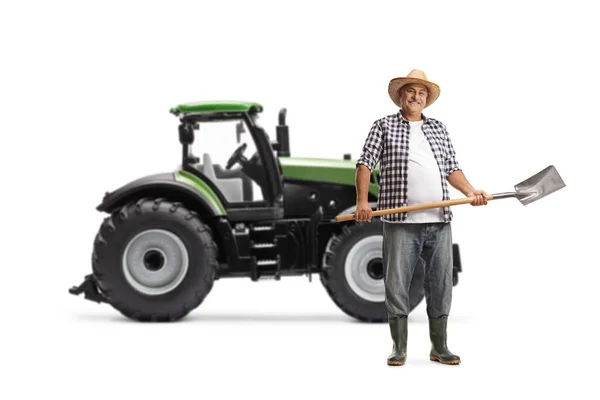 白い背景に隔離された緑のトラクターの前にシャベルを持つ成熟した農家の完全な長さの肖像画 — ストック写真