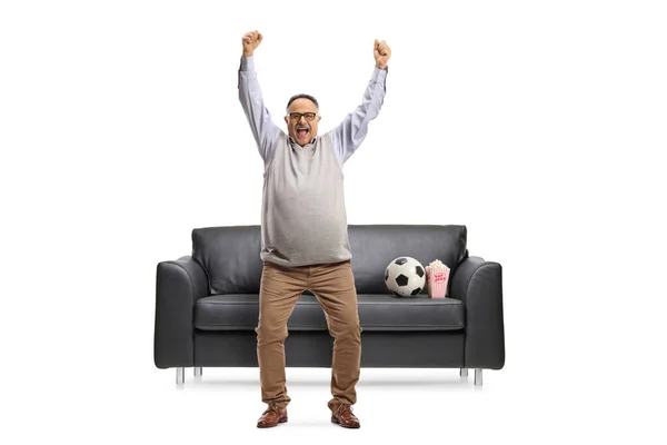 一个快乐而成熟的足球迷在白色背景的沙发前欢呼的全长肖像 — 图库照片
