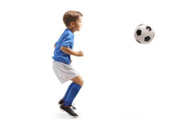 Beyaz arka planda izole edilmiş bir futbol topuyla atlayan küçük bir çocuğun tam boy profil çekimi.