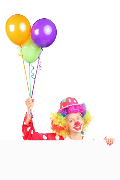 Female clown holding balloons behind panel — Stock Photo, Image