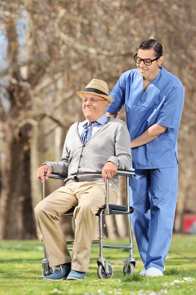 Homme infirmier poussant senior en fauteuil roulant — Photo
