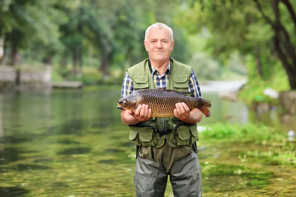 Äldre fiskare i floden håller fisk — Stockfoto