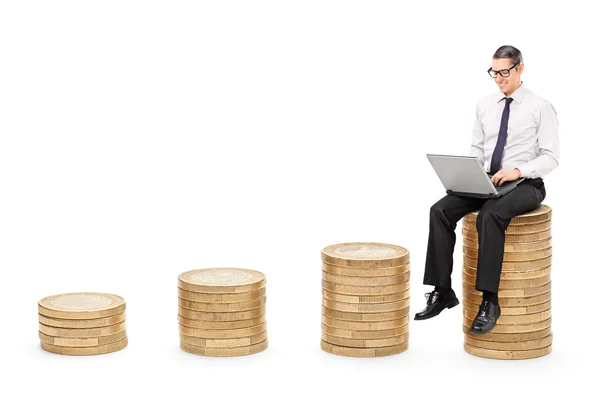 Man working on laptop seated on coins — Stock Photo, Image