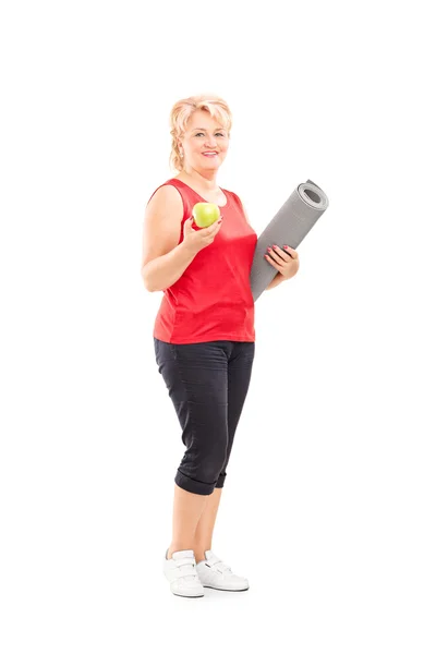 Mujer madura sosteniendo manzana y estera — Foto de Stock