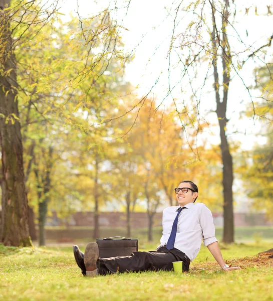 Üzletember pihentető ül a füvön, a park — Stock Fotó