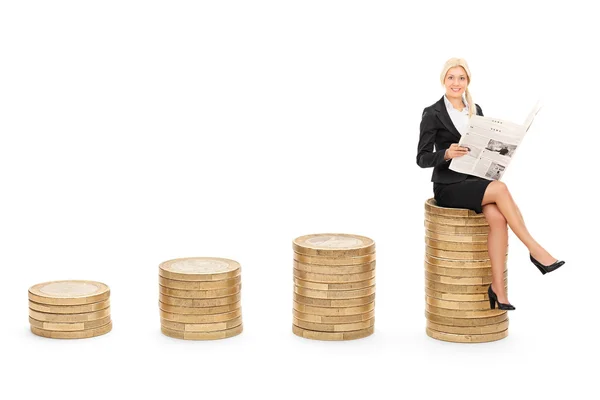 Businesswoman reading news seated on coins — Stock Photo, Image