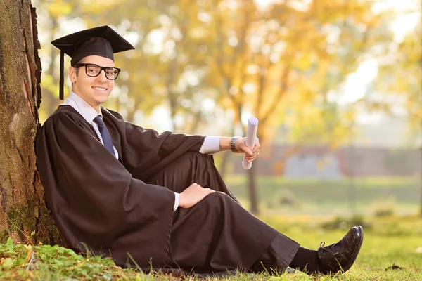 Afgestudeerde student zitten door boom — Stockfoto